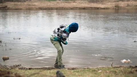 A boy throws stones from the river Bank into the water Stock Footage 128016494