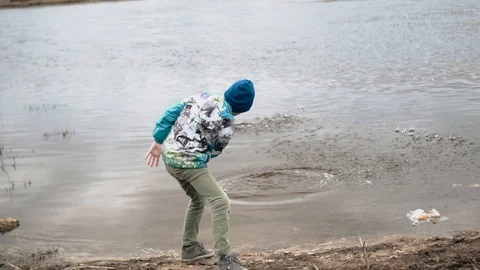The boy throws stones into the water making them jump on the surface Stock Footage 128016508