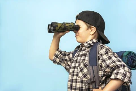 Boy tourist looks through binoculars on a blue background, copy space Stock Photos