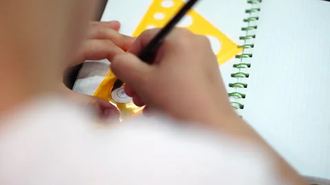 Boy tracing a round stencil on a triangle with a simple pencil in a notebook in  Video stock 307121725