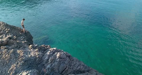 Boy in trunks diving from a cliff into the sea Stock Footage 108110290
