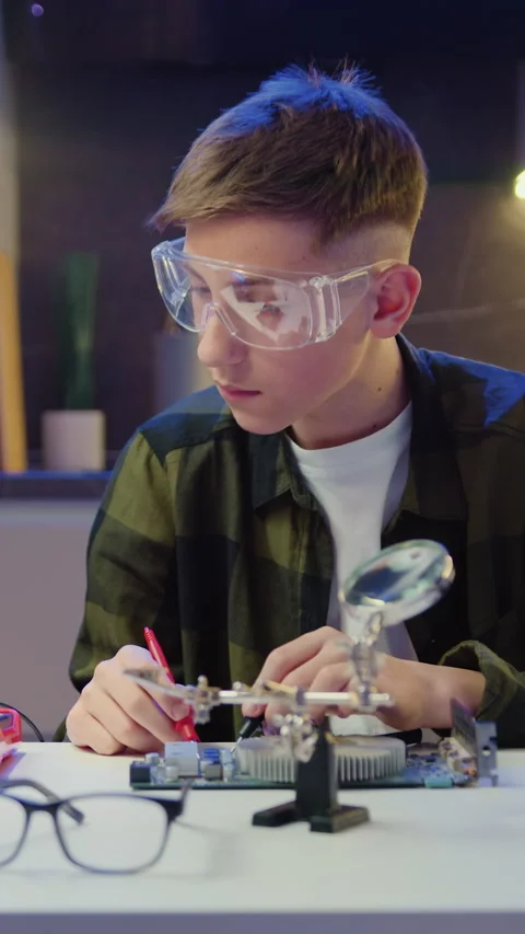 Boy try to fixing computer board in school science club. Male teen unscrews chip Stock Footage 327372964