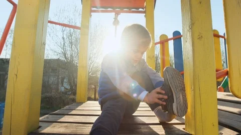 Boy trying to put on shoes on playground outdoor at sunset. 動画素材 128440135