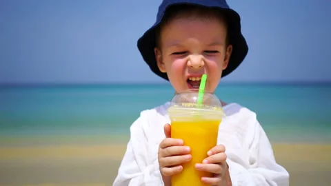 Boy of two years drinking mango fresh on the beach on the background of the Stock Footage 88379503