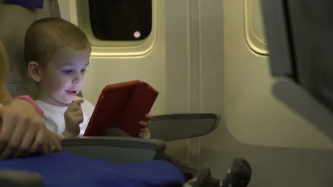 Boy two years old playing on a tablet app, and sit in the aircraft seat. Stock Footage 88411754