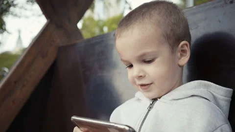 Boy of two years sitting on a bench in the park and watching cartoons on a Stock Footage 90973941