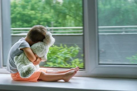 Boy of two years sitting by the window and hugs a toy Bunny. rainy weather Foto stock