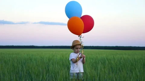 Boy of two years standing in the field and releasing balloons into the sky Stock Footage 92339376