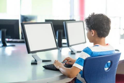 Boy typing on keyboard at round table in school computer lab among three Stock Photos