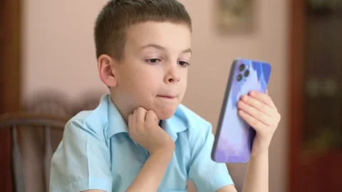 Boy typing text message by smartphone at home. A schoolboy holds a modern phone Stock Footage 236229022