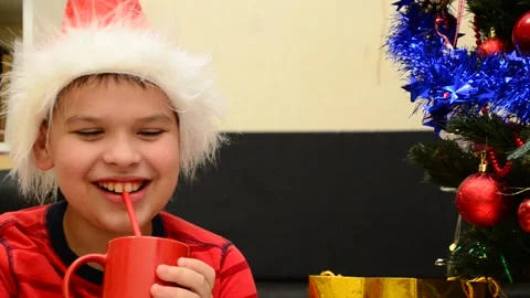 Boy under Christmas tree at home drink hot chocolate open presents 動画素材 166552687