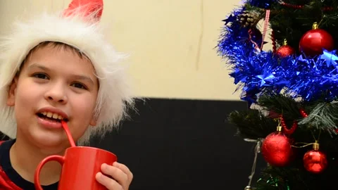 Boy under Christmas tree at home drink hot chocolate open presents 動画素材 166552708