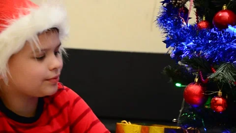 Boy under Christmas tree at home drink hot chocolate open presents 動画素材 166552735