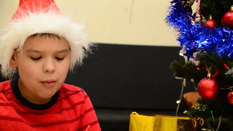 Boy under Christmas tree at home drink hot chocolate open presents 動画素材 166552755