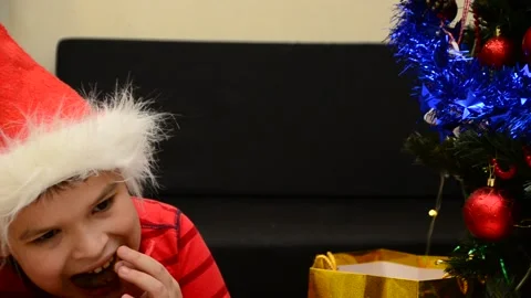 Boy under Christmas tree at home drink hot chocolate open presents 動画素材 166552756