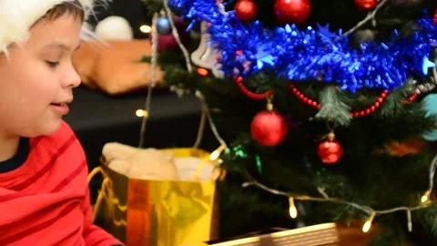 Boy under Christmas tree at home. Little boy in knitted sweater with Xmas orname 動画素材 166552804
