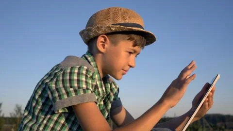 Boy use tablet sitting in field at sunset Stock Photos