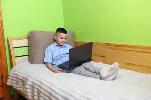 A boy uses a laptop while lying on the couch. Stock Photos