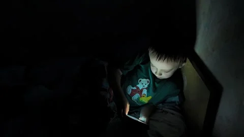 Boy uses smartphone in dark room while sitting on bed at night Stock Footage 338437926