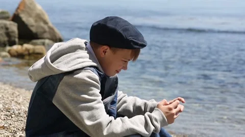 Boy uses a smartphone while sitting on the beach in spring day Video stock 49922456