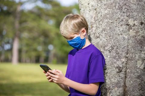 Boy using cell phone while wearing homemade face mask for protection Stock Photos