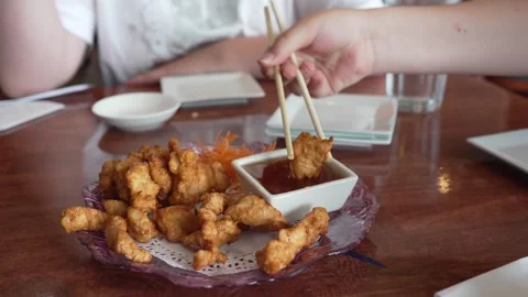 Boy using chopsticks to dip crispy chicken karaage in sauce at restaurant Stock Footage 336278707