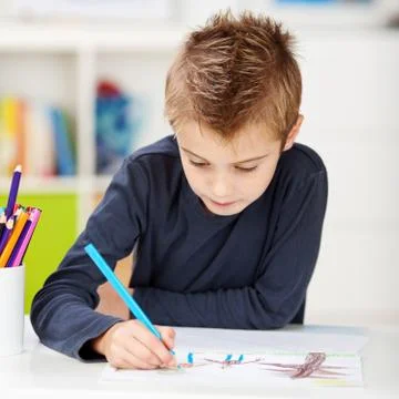 Boy using colored pencil while drawing on paper at table Stock Photos
