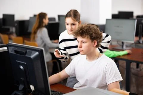 Boy using computer to help girl to solve problem in classroom 写真素材