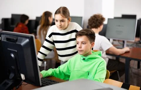 Boy using computer to help girl to solve problem in classroom Stock Photos