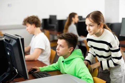 Boy using computer to help girl to solve problem in classroom Stockfoto's