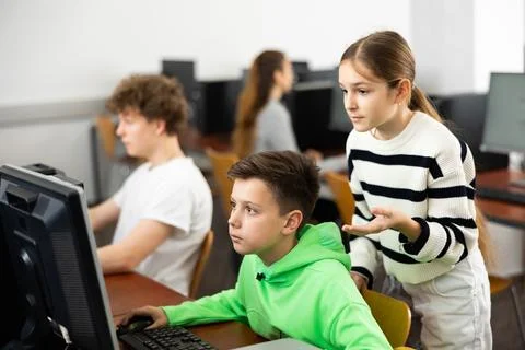 Boy using computer to help girl to solve problem in classroom Stock Photos