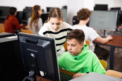 Boy using computer to help girl to solve problem in classroom Stockfoto's