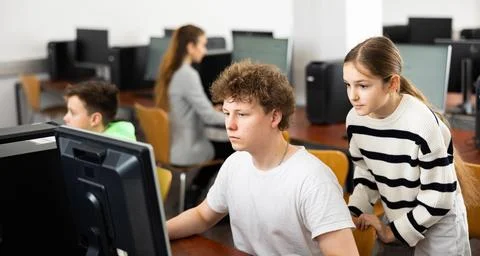 Boy using computer to help girl to solve problem in classroom 写真素材