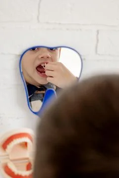 Boy using dental floss pick in mirror. He has bad teeth with cavities. Stock Photos