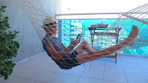 Boy using digital tablet computer lying in the hammock hanging on balcony of Stock Footage 134481962