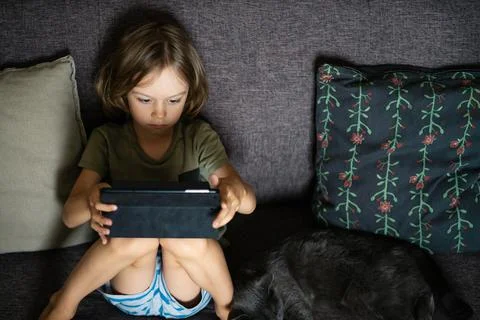 Boy using digital tablet computer playing games or watching cartoons at home. Stock Photos