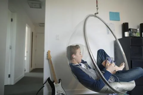 Boy using digital tablet headphones hanging bubble chair Stock Photos