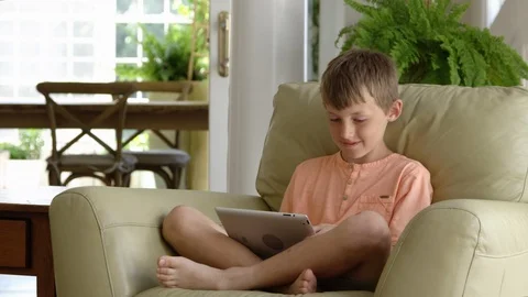 Boy using digital tablet sitting on armchair 動画素材 88011607