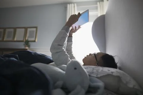 Boy using digital tablet upside-down in bed Stock Photos