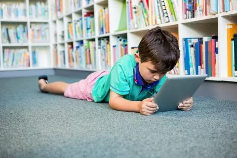 Boy using digital tablet while lying in school library 스톡 사진
