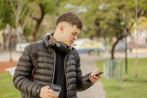 Boy using his mobile phone while walking through a public park. Stockfoto's