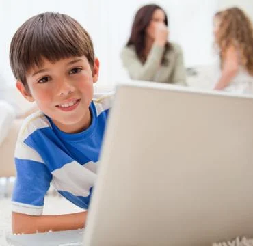 Boy using laptop on the carpet with his family behind him Stock Photos