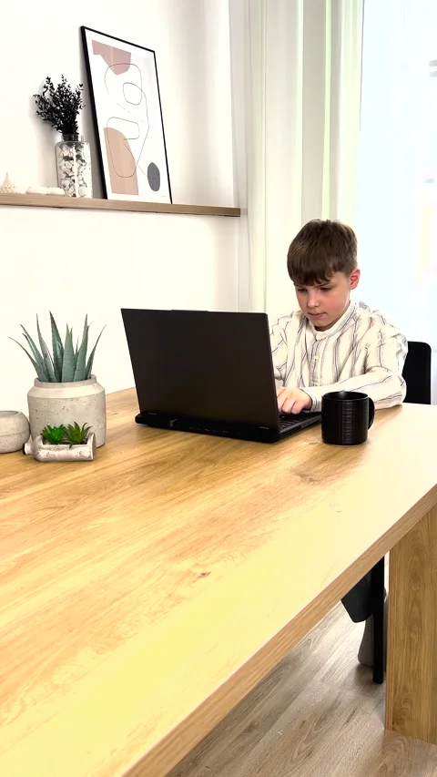 A boy is using a laptop computer at a table, surrounded by houseplants. Vertical Stock Footage 272751630