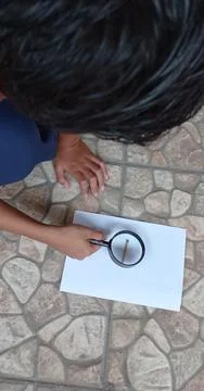 A boy is using a loop to burn a white sheet of paper Stock Photos