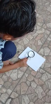 A boy is using a loop to burn a white sheet of paper by the sun's power Stock Photos