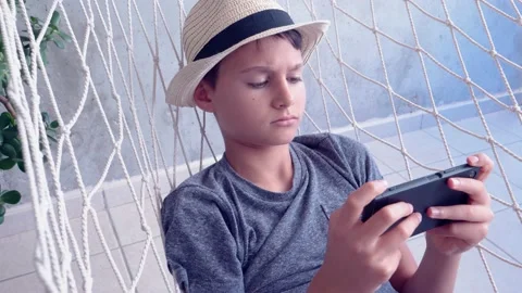 Boy using mobile phone lying in the hammock hanging on balcony of apartment. 4k 動画素材 133371665