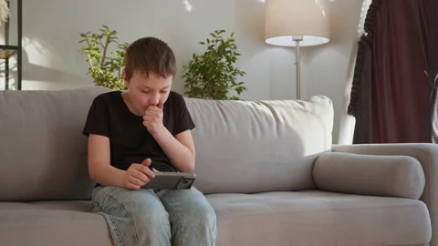 Boy Using Mobile Phone on Sofa. Thoughtful child digital focus relaxed home Stock Footage 335477933