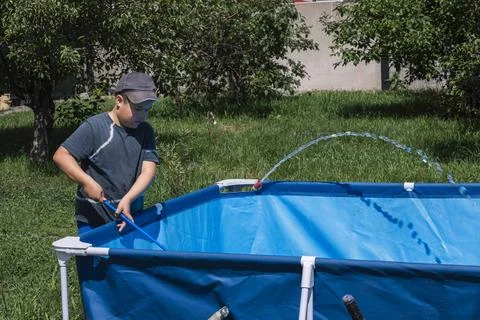 Boy using a net to remove debris from a vibrant blue pool, illustrating the Stock Photos