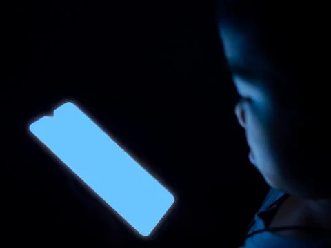 A boy is using a phone with a blank blue screen on a dark black background.. Foto stock