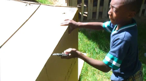 Boy using small saw to cut a cardboard box Stock Footage 27735933